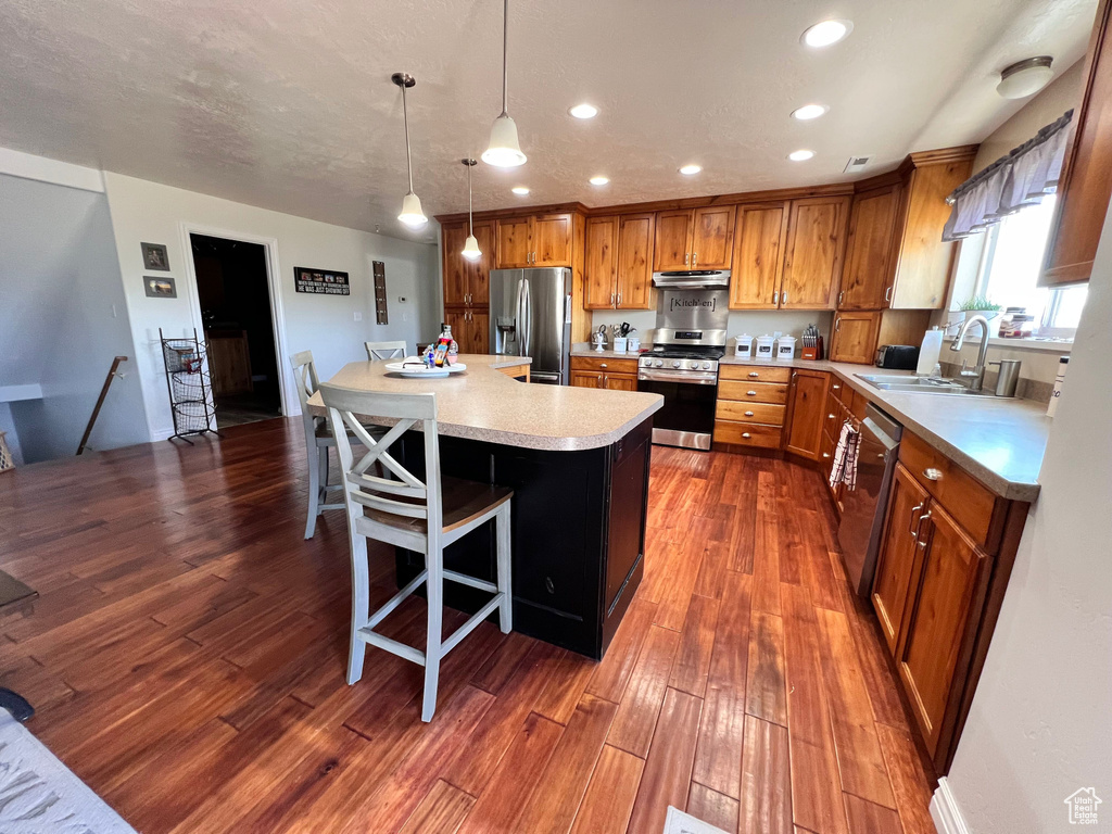 Kitchen with appliances with stainless steel finishes, under cabinet range hood, light countertops, brown cabinetry, and a sink
