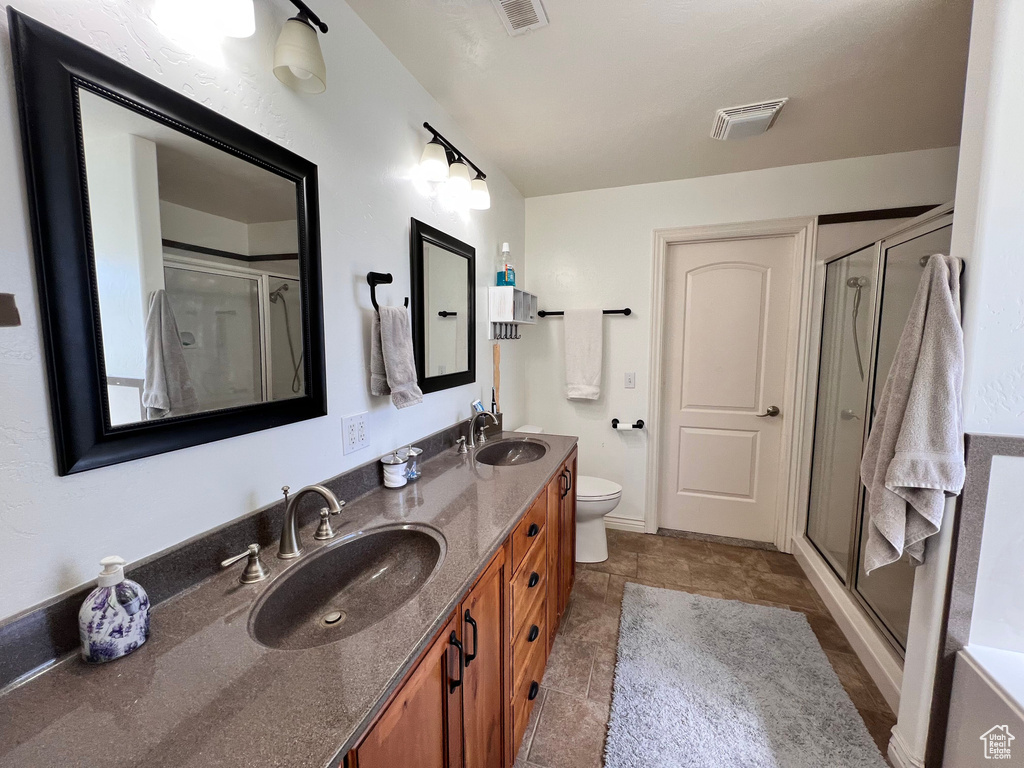 Full bathroom featuring double vanity, a stall shower, and toilet