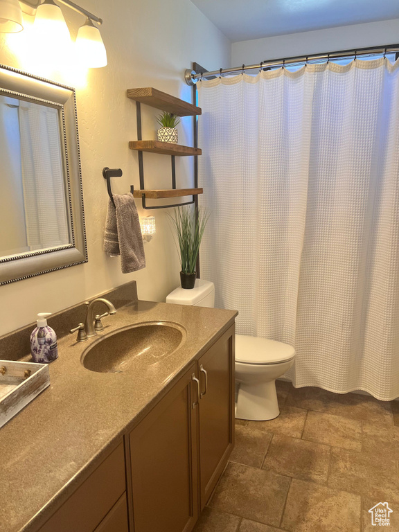 Full bathroom featuring stone finish floors, vanity, toilet, and curtained shower