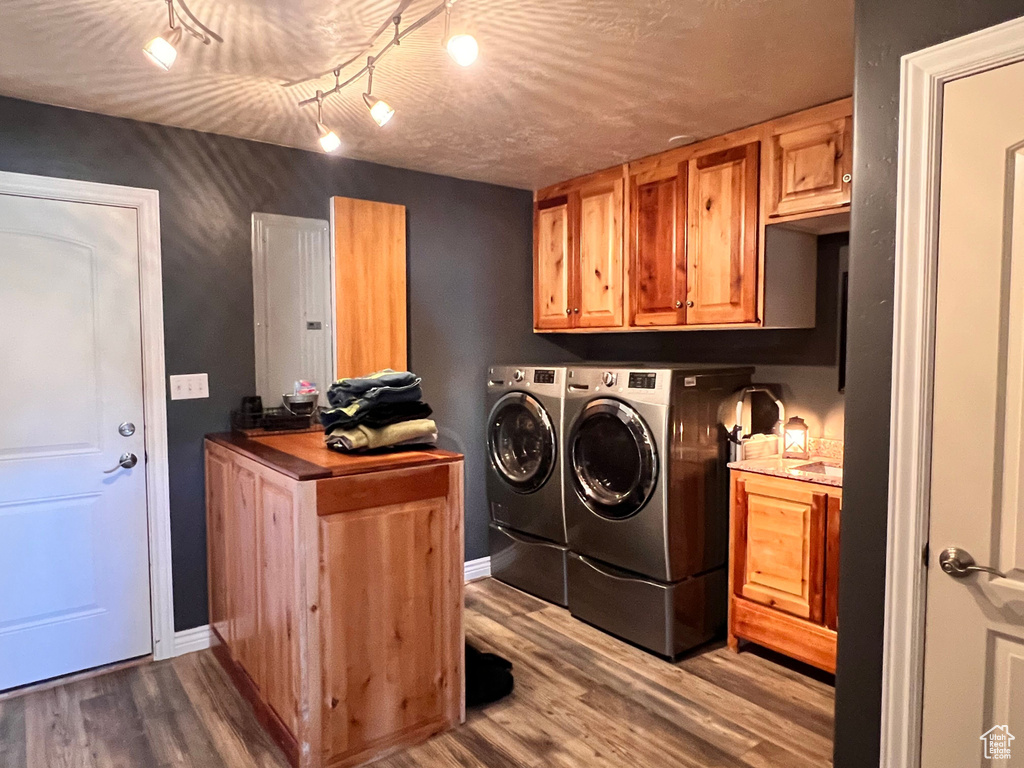 Washroom featuring washer and dryer, electric panel, cabinet space, and wood finished floors