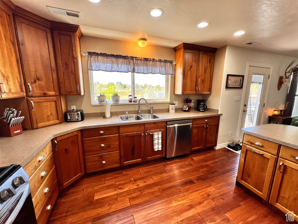 Kitchen with stainless steel appliances, a sink, dark wood-type flooring, brown cabinetry, and recessed lighting