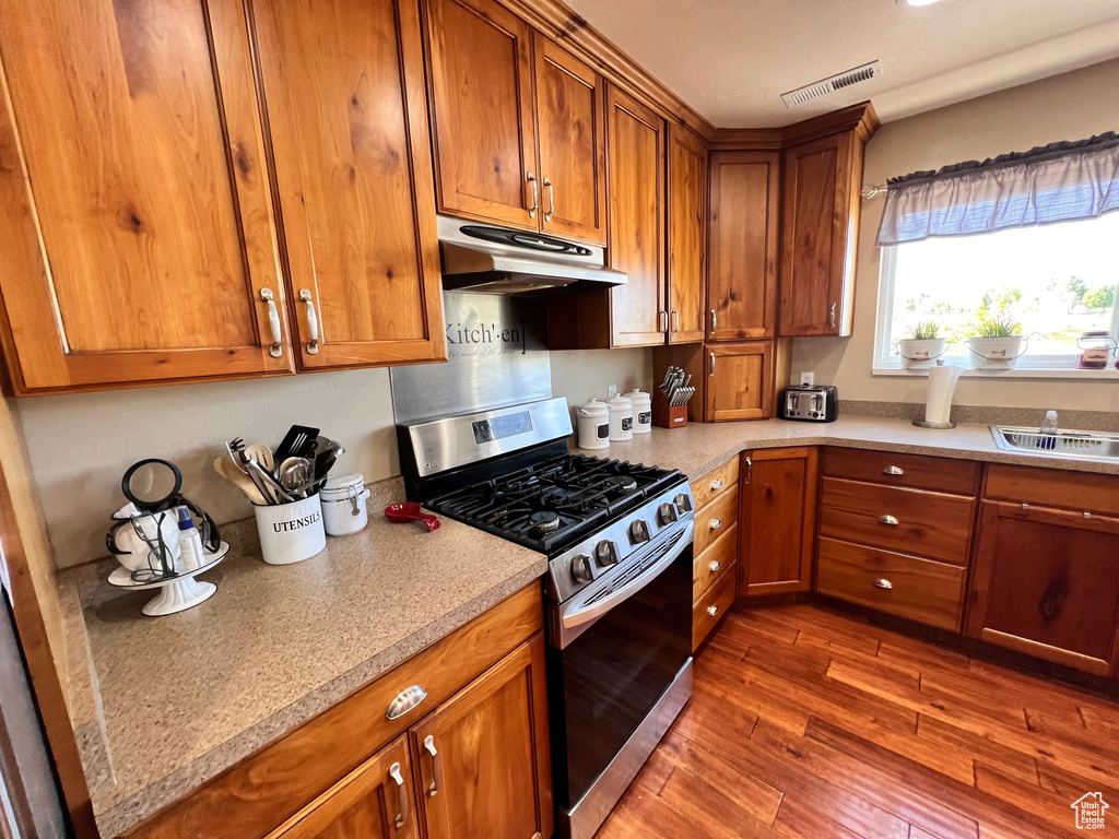 Kitchen featuring stainless steel gas range oven, under cabinet range hood, brown cabinets, and wood finished floors