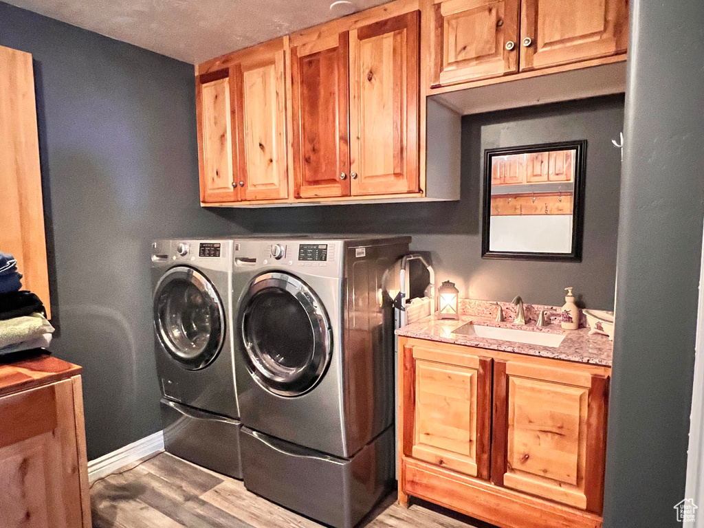Washroom featuring cabinet space, separate washer and dryer, light wood-type flooring, and baseboards