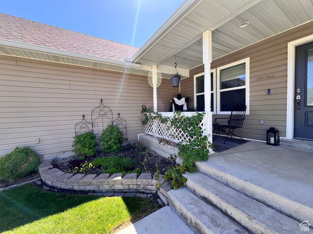 Property entrance featuring covered porch and a shingled roof