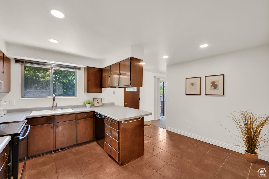 Kitchen with black appliances, a sink, a peninsula, light countertops, and healthy amount of natural light