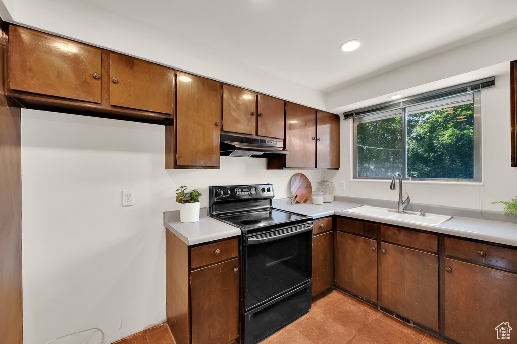 Kitchen with black range with electric cooktop, a sink, under cabinet range hood, light countertops, and light tile patterned floors
