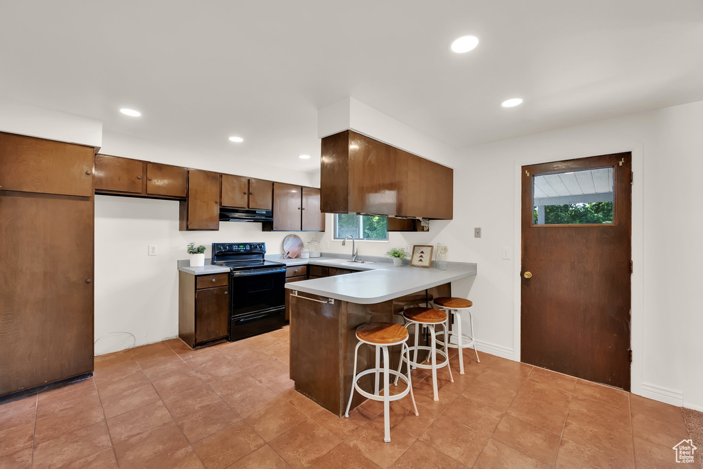 Kitchen featuring black electric range oven, extractor fan, a sink, a peninsula, and a breakfast bar