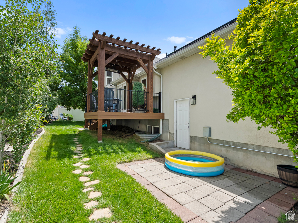 View of grassy yard featuring a pergola, a wooden deck, and a patio area