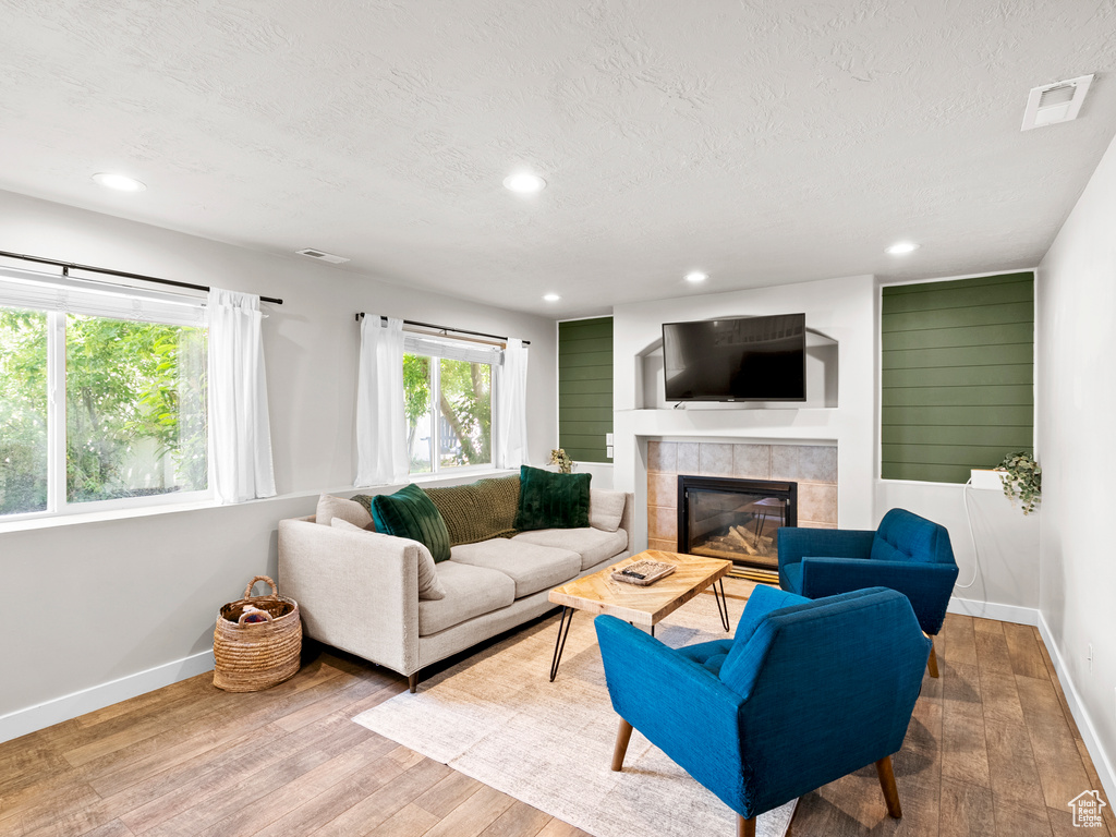 Living area featuring wood finished floors, a fireplace, baseboards, a textured ceiling, and recessed lighting