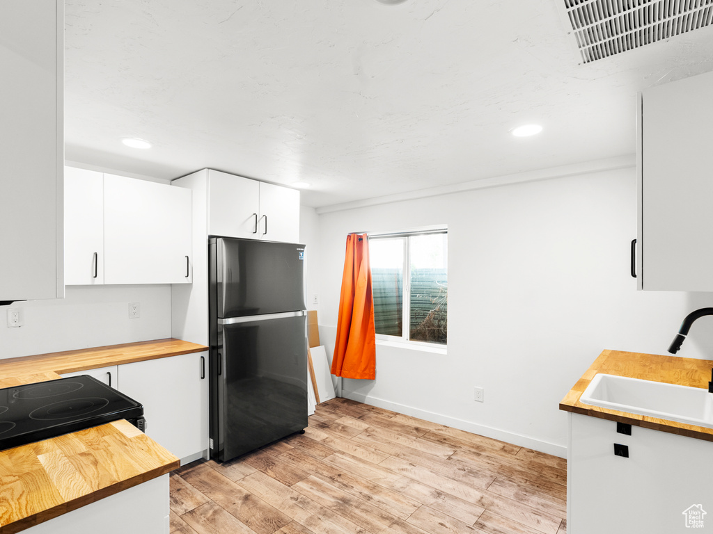 Kitchen with freestanding refrigerator, wooden counters, a sink, light wood-style floors, and baseboards