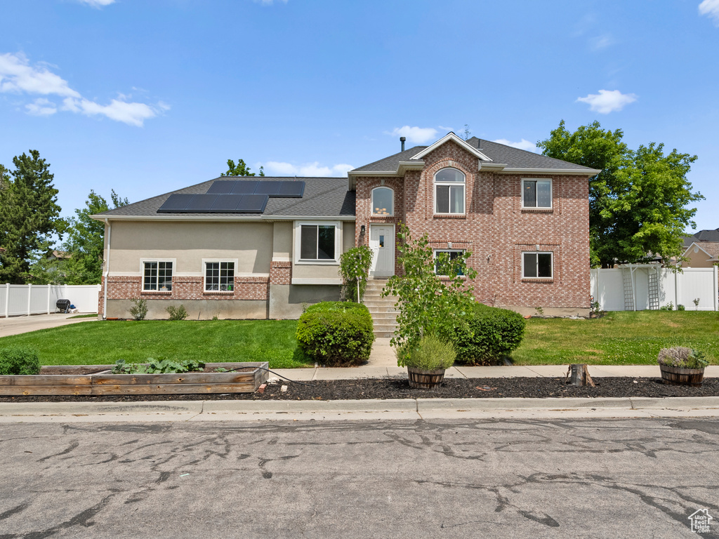 View of front of home with solar panels, brick siding, and roof with shingles