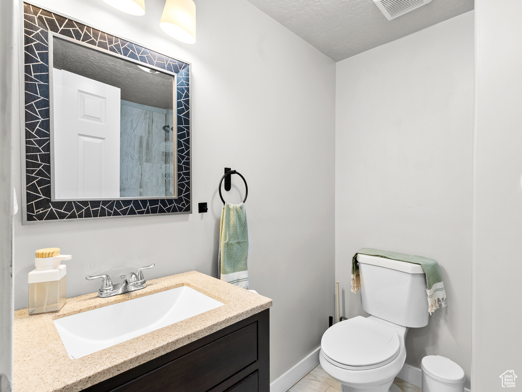 Full bath with vanity, toilet, a textured ceiling, baseboards, and a shower