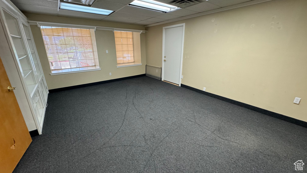 Unfurnished room with baseboards, a drop ceiling, and dark carpet