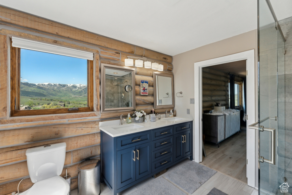 Bathroom featuring log walls, double vanity, a shower with door, and toilet
