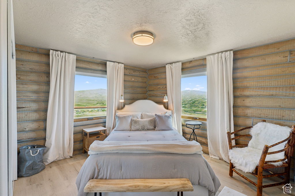 Bedroom with log walls, light wood-style flooring, and a textured ceiling