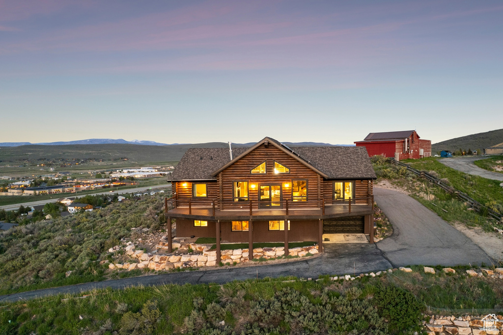 Back of house at dusk featuring a shingled roof, log exterior, and a deck with mountain view