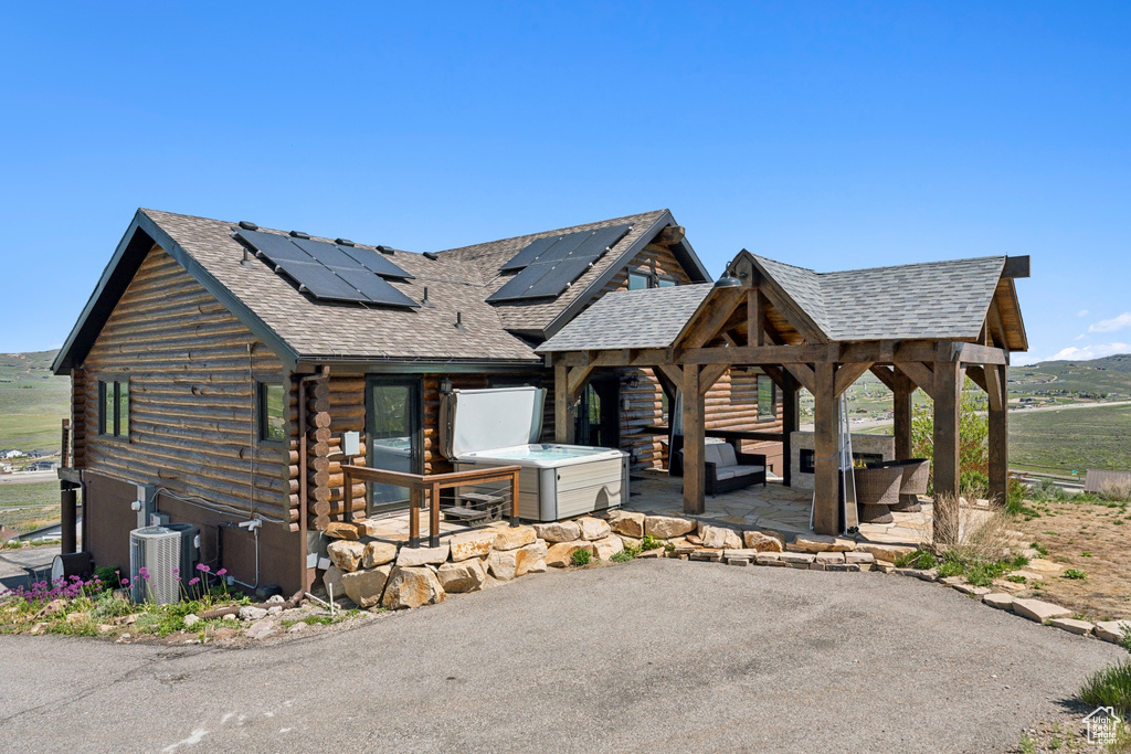 View of front facade featuring roof with shingles, log siding, solar panels, a patio area, and central air condition unit