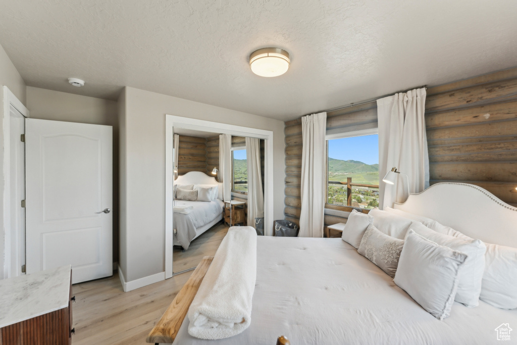 Bedroom featuring light wood-style floors, log walls, baseboards, a mountain view, and a textured ceiling
