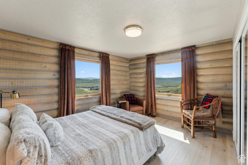 Bedroom featuring log walls, wood finished floors, and a textured ceiling