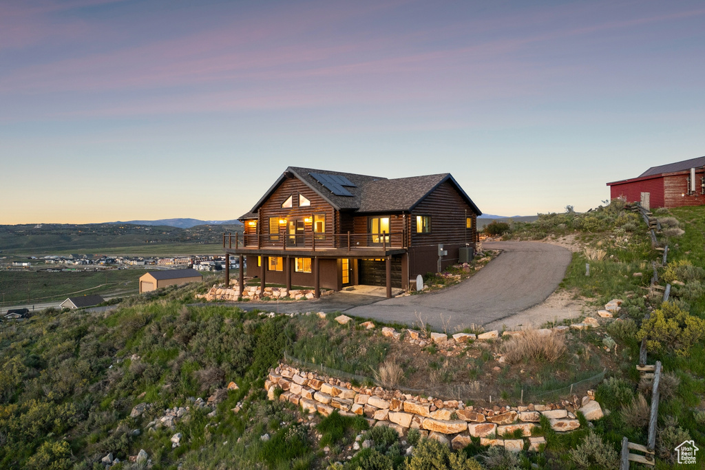 Back of property at dusk featuring a wooden deck, log exterior, solar panels, and roof with shingles