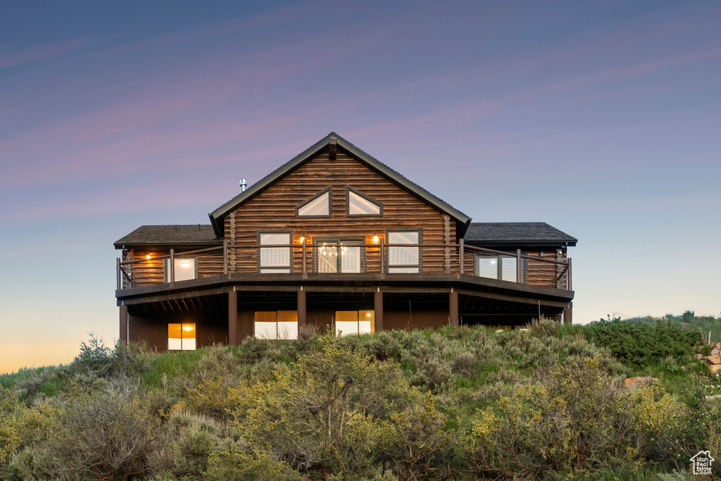 Back of property at dusk with a balcony, log exterior, and roof with shingles