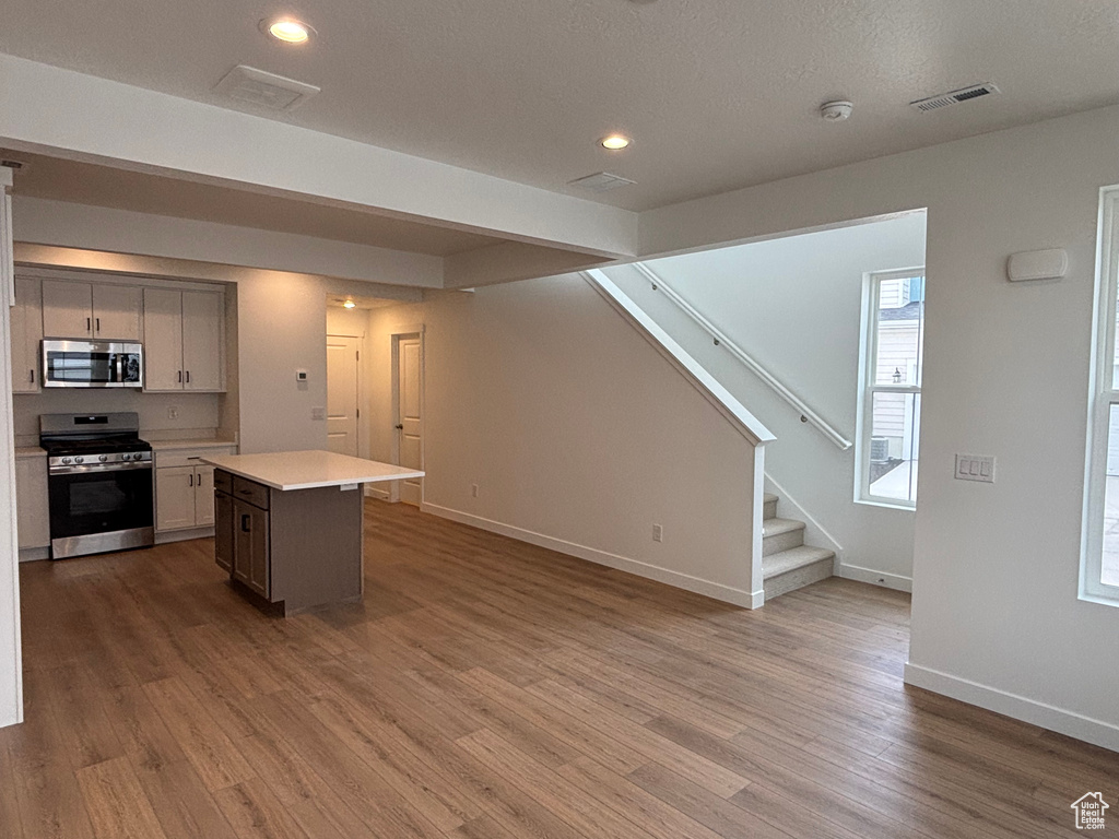 Kitchen with stainless steel appliances, light countertops, a center island, recessed lighting, and wood finished floors