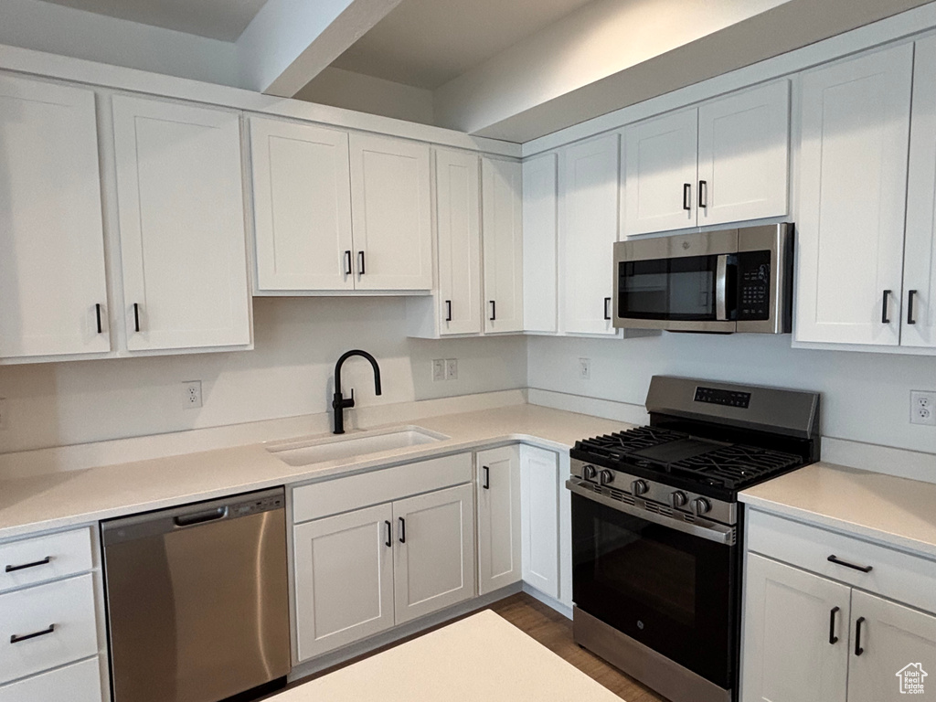 Kitchen with stainless steel appliances, a sink, white cabinets, light countertops, and dark wood-style flooring