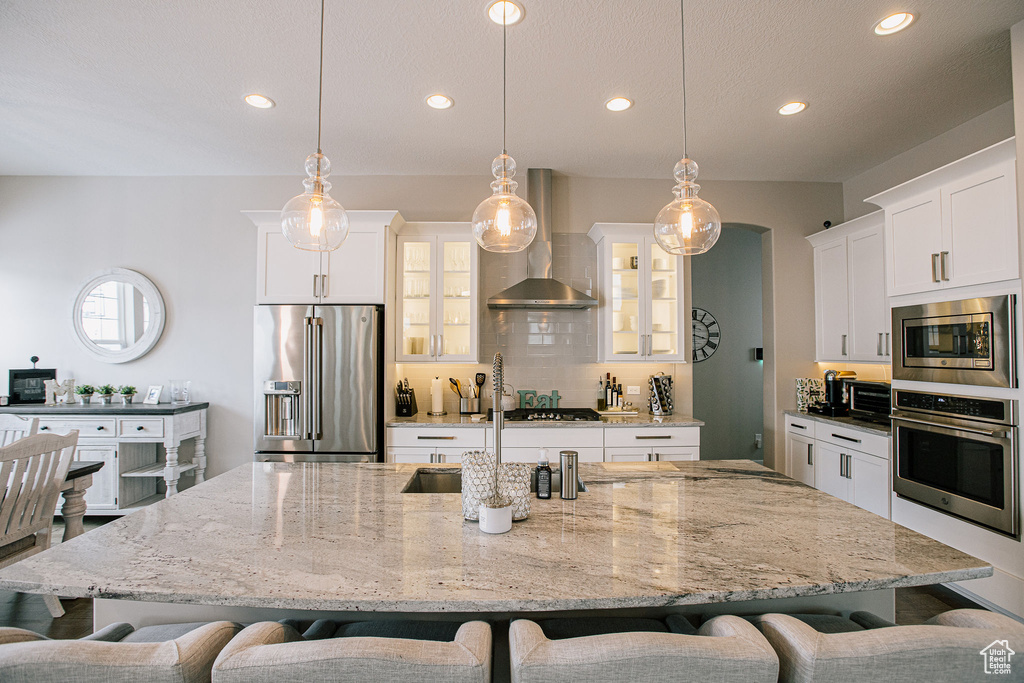 Kitchen with appliances with stainless steel finishes, wall chimney exhaust hood, a breakfast bar, recessed lighting, and glass insert cabinets