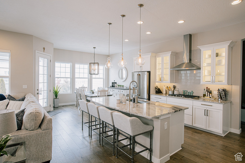 Kitchen with wall chimney range hood, a sink, appliances with stainless steel finishes, a breakfast bar, and open floor plan