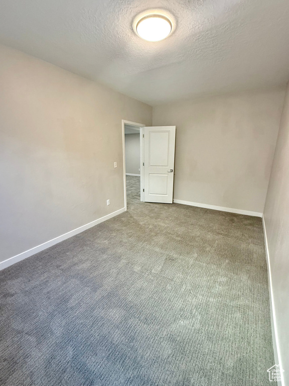 Carpeted empty room featuring a textured ceiling and baseboards