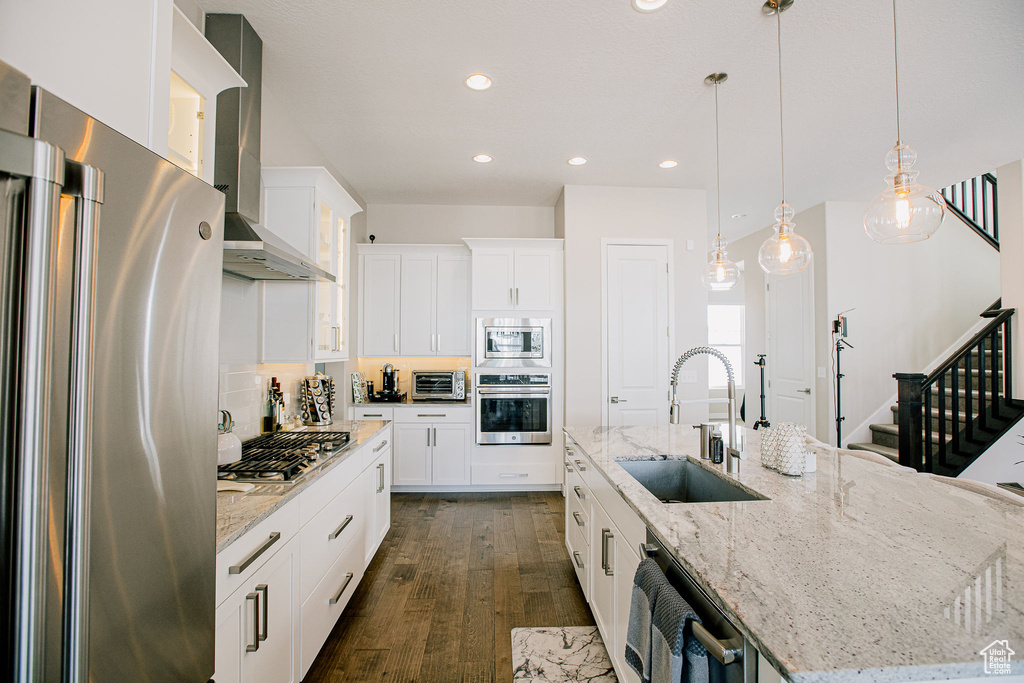 Kitchen featuring stainless steel appliances, a sink, wall chimney exhaust hood, a spacious island, and dark wood-type flooring