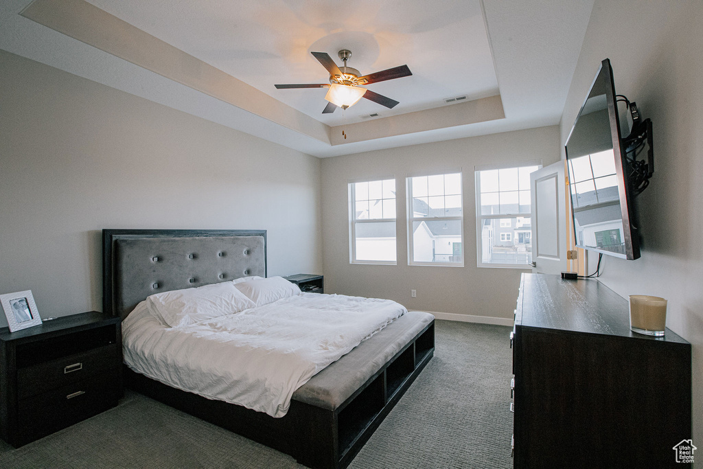 Bedroom featuring dark carpet, a tray ceiling, baseboards, and a ceiling fan