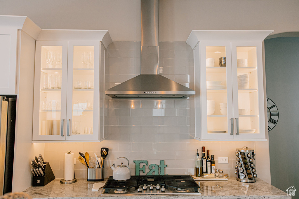 Kitchen featuring wall chimney exhaust hood, stainless steel gas cooktop, tasteful backsplash, light stone countertops, and arched walkways