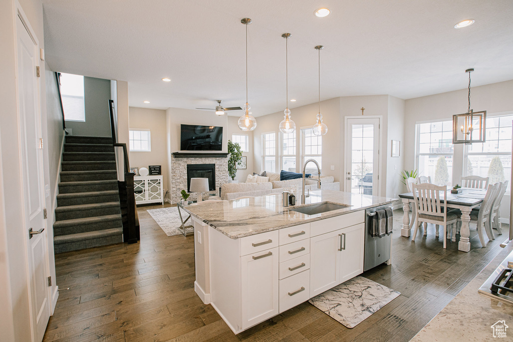 Kitchen with a sink, a fireplace, dark wood-type flooring, ceiling fan, and light stone countertops