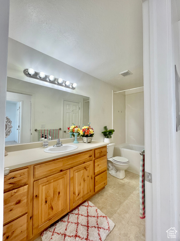 Bathroom featuring vanity, toilet, tile patterned floors, shower / bathtub combination, and a textured ceiling