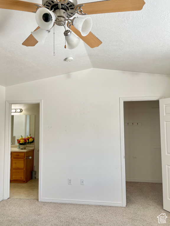 Unfurnished bedroom featuring a spacious closet, light carpet, vaulted ceiling, ensuite bathroom, and ceiling fan