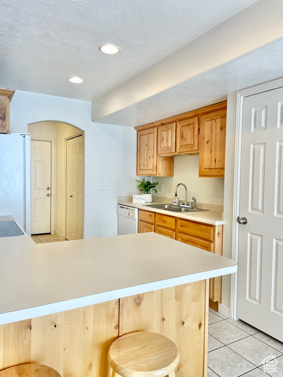 Kitchen featuring white appliances, light countertops, light tile patterned floors, a breakfast bar, and a sink