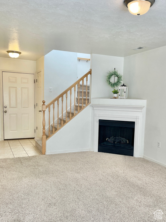 Unfurnished living room with carpet floors, a textured ceiling, stairs, a fireplace, and baseboards