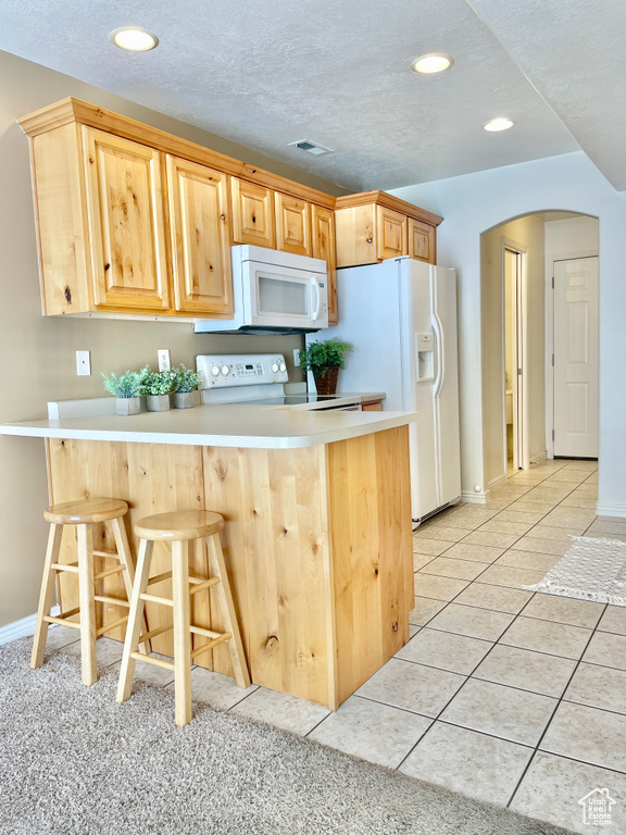Kitchen featuring white appliances, arched walkways, a peninsula, a breakfast bar area, and light brown cabinets