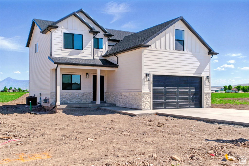View of front of house with board and batten siding, a garage, stone siding, and concrete driveway