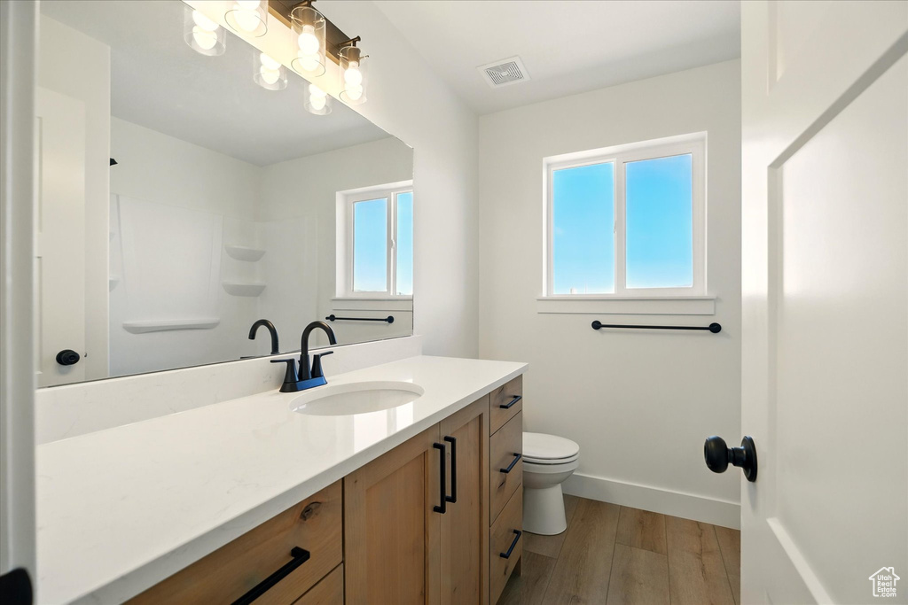 Full bathroom with plenty of natural light, vanity, wood finished floors, and toilet
