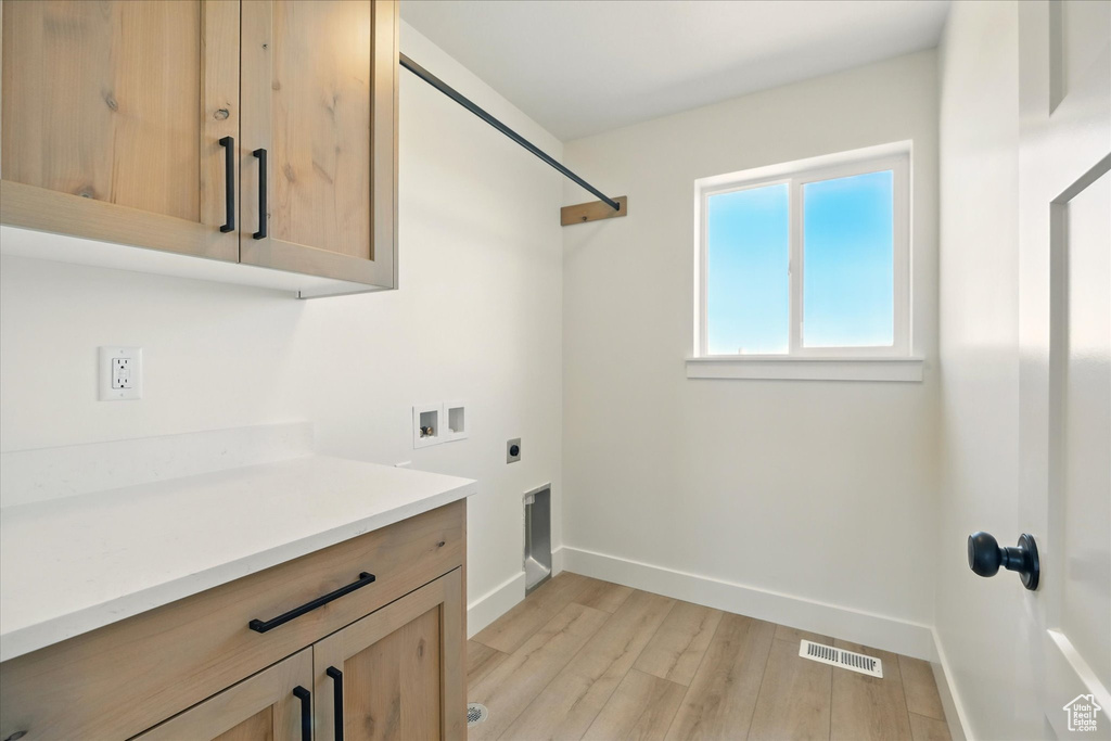 Washroom featuring cabinet space, hookup for a washing machine, electric dryer hookup, baseboards, and light wood-style flooring