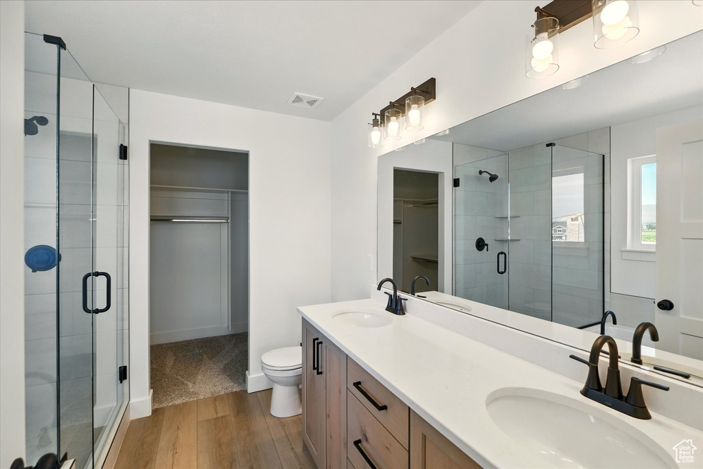 Bathroom featuring a walk in closet, wood finished floors, a stall shower, double vanity, and toilet
