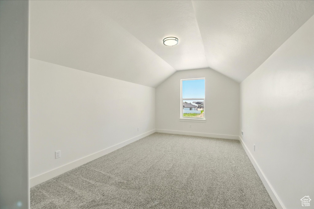 Additional living space with light colored carpet, vaulted ceiling, and baseboards