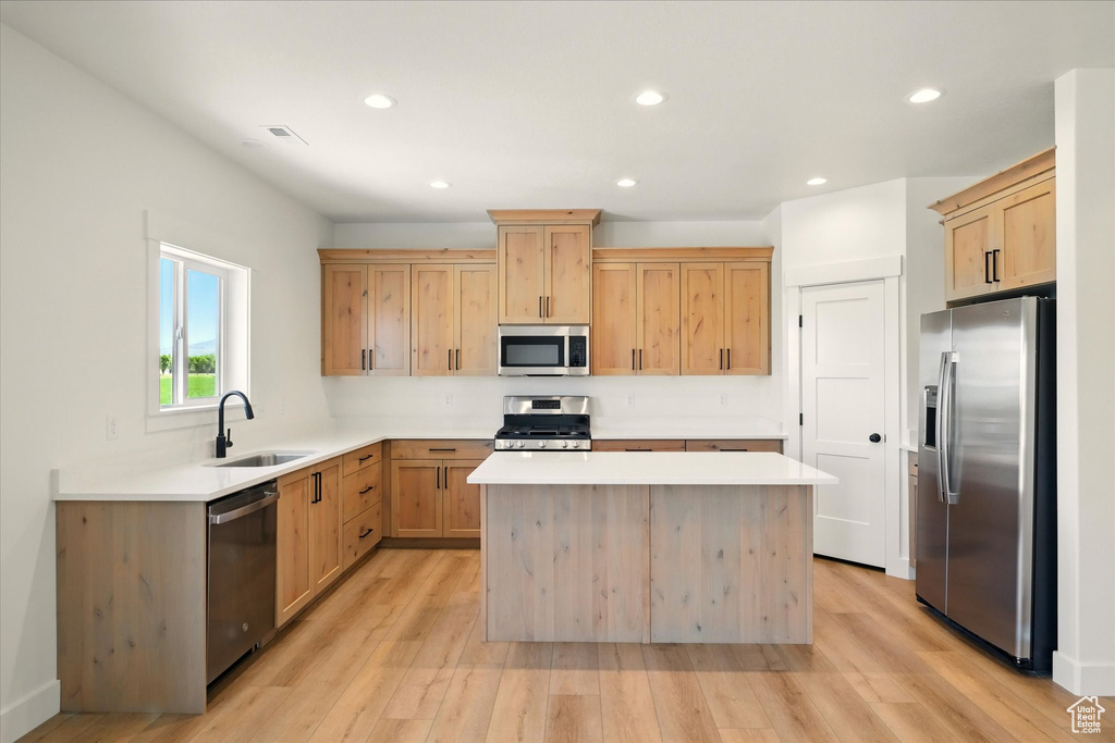Kitchen featuring stainless steel appliances, a sink, light brown cabinetry, a center island, and light countertops