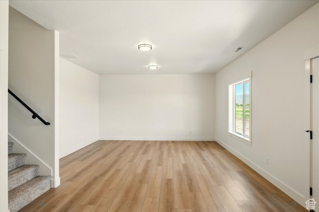 Spare room with light wood-type flooring, baseboards, and stairway