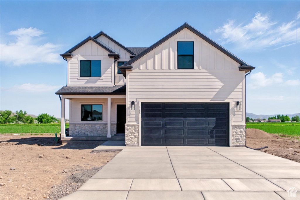 View of front facade with board and batten siding, stone siding, concrete driveway, a garage, and covered porch