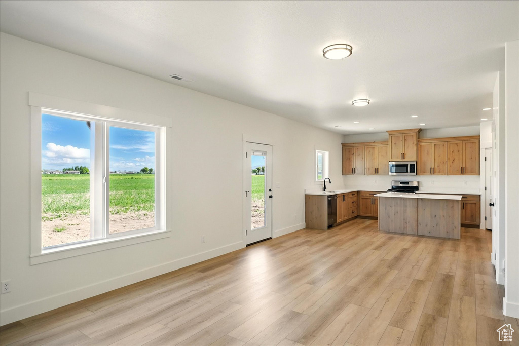 Kitchen with appliances with stainless steel finishes, light countertops, light wood-type flooring, a center island, and baseboards