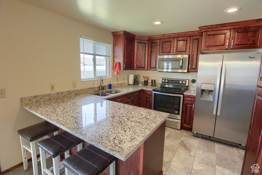 Kitchen with appliances with stainless steel finishes, a sink, a peninsula, a breakfast bar, and dark brown cabinets