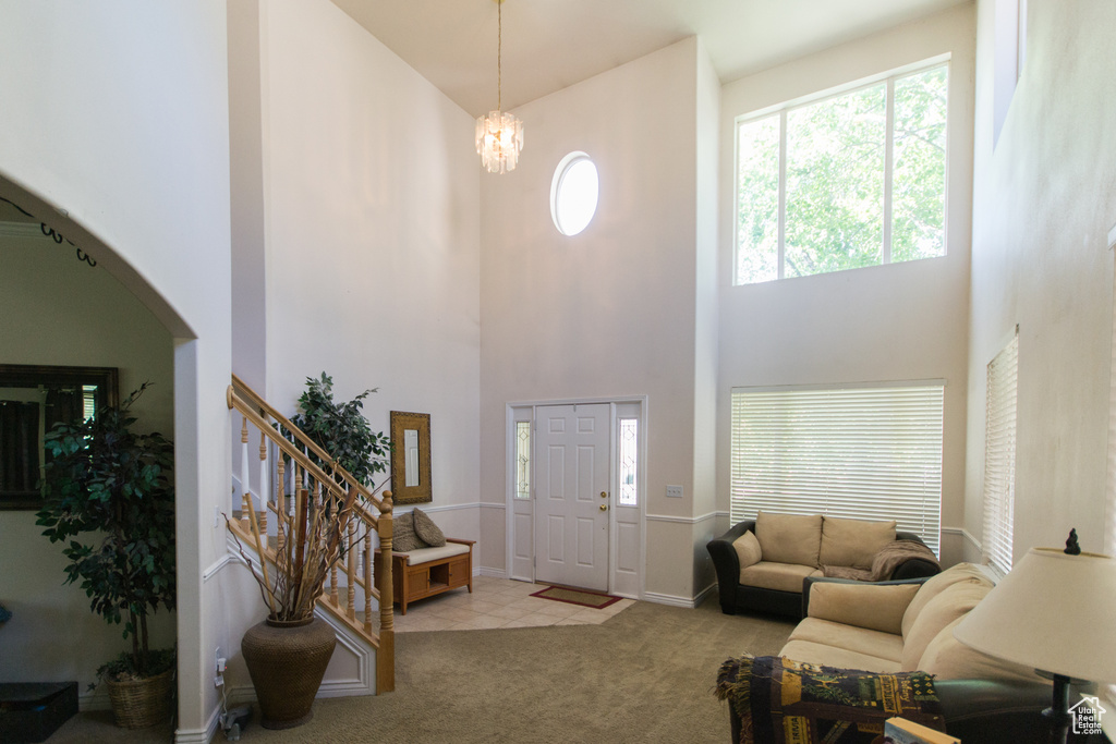 Carpeted foyer entrance featuring a towering ceiling, stairway, arched walkways, a chandelier, and baseboards